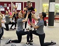  Cheer team members hold up a Mini-Cardinals cheerleader at practice.